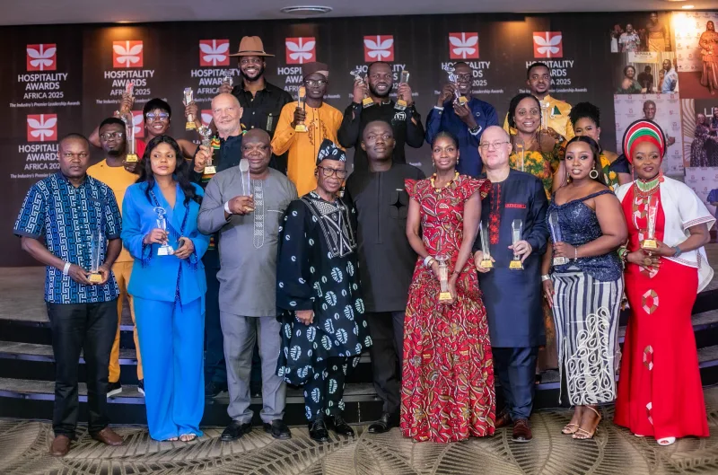 Les lauréats des Hospitality Awards Africa 2025 sur scène avec leurs trophées, devant le mur des prix