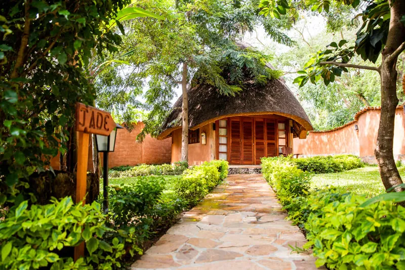Une allée dallée entre des haies taillées menant au bungalow Jade, une lanterne et un panneau en bois sculpté au tournant