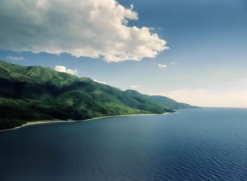 Green mountains falling to a narrow sand shoreline along the deep blue water of Lake Tanganyika