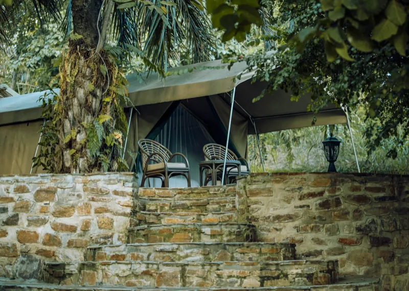 Une tente en toile avec fauteuils en rotin, derrière un muret de pierre sèche incurvé