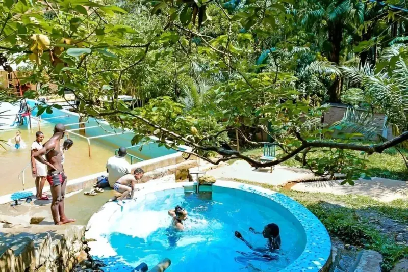 Visitors bathing in the warm turquoise pools of the Mugara hot springs, shaded by overhanging trees