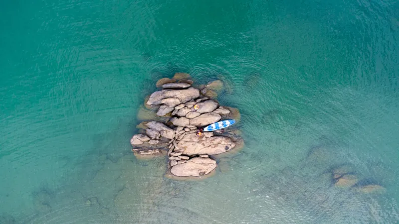 Une planche de paddle près d’un affleurement rocheux dans l’eau turquoise et limpide du lac Tanganyika, vue du ciel