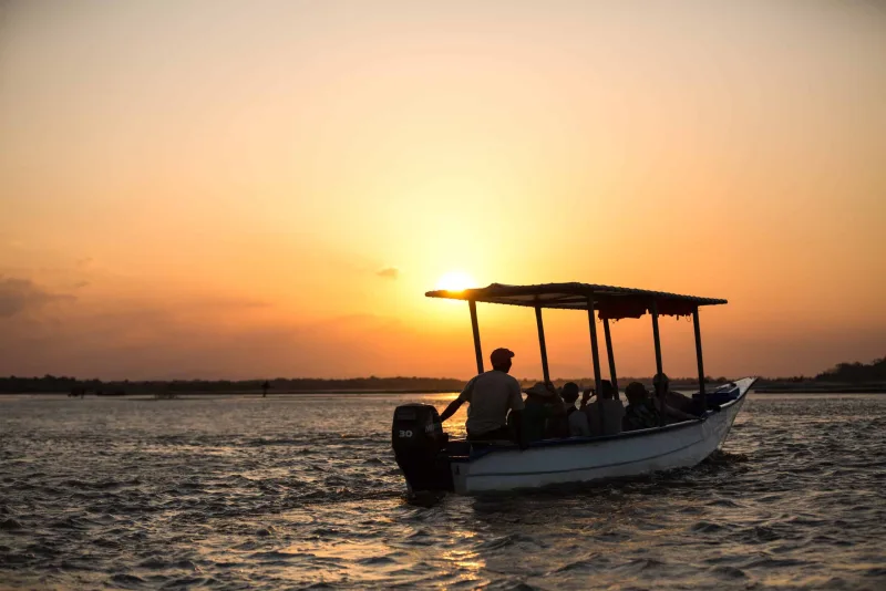 A covered boat carrying guests across Lake Tanganyika as the sun drops to the horizon