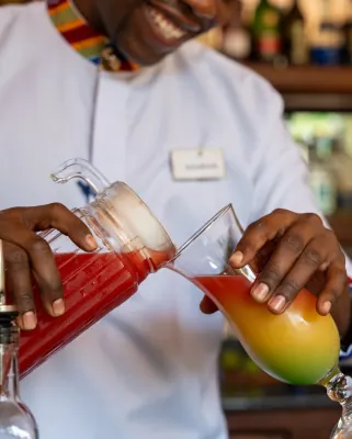 A bartender pouring a layered red and gold cocktail from a jug into a glass