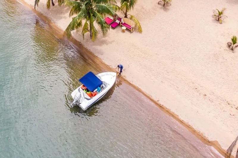 An aerial view of a boat transfer arriving at the white sand beach, with loungers set out along the shore