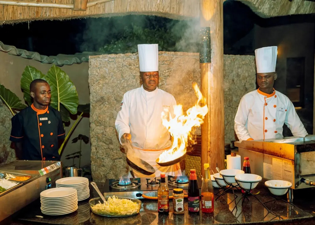 Two chefs in whites working a live cooking station, flames rising from the pan