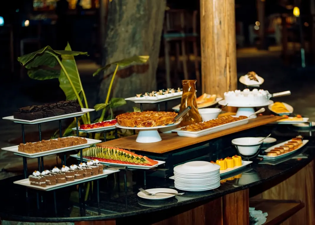 A dessert buffet laid along a curved counter: cakes, tarts and small pastries under warm light