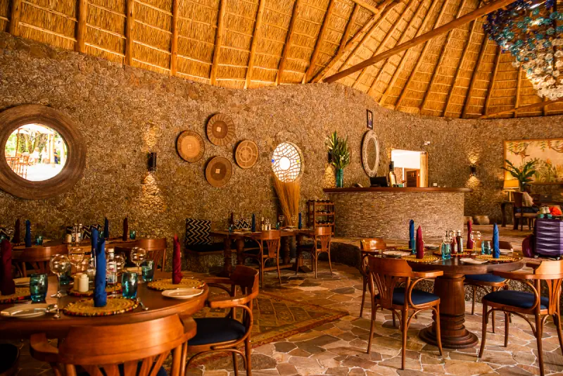 The round dining room under its thatched roof, stone walls hung with woven baskets and tables laid for dinner