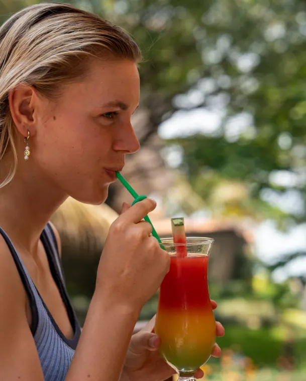 A guest drinking a layered cocktail through a straw, green garden out of focus behind her