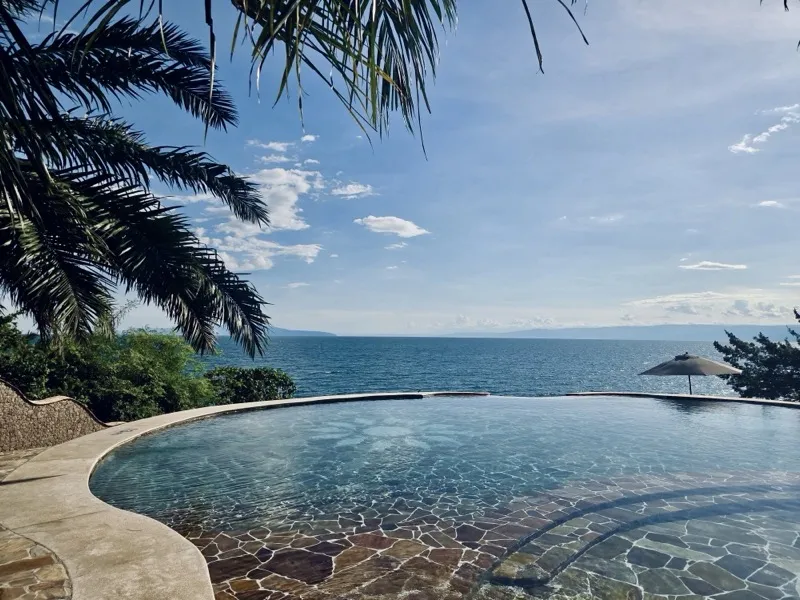 Le rebord incurvé en pierre de la piscine à débordement sous les palmes, face au lac Tanganyika et aux montagnes de la rive opposée