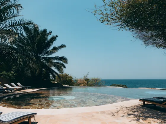 The round infinity pool under the palms, loungers around its edge and the lake beyond