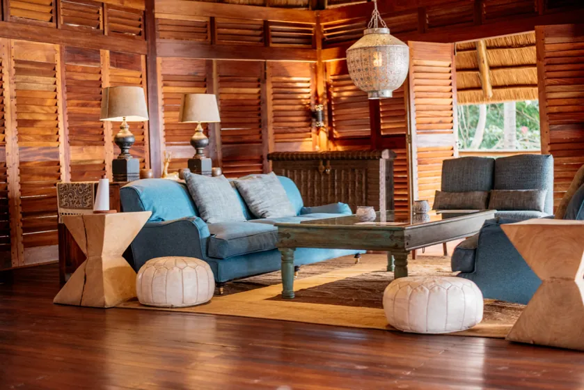 Blue sofas, leather poufs and a pendant lamp in a lounge lined with wooden louvred shutters