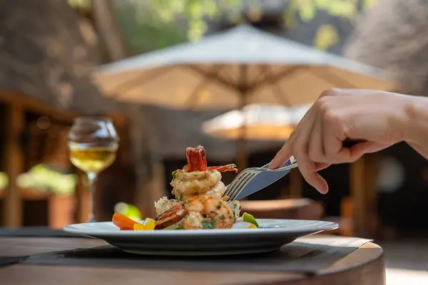 A plated prawn dish on a shaded terrace table, a glass of white wine beside it