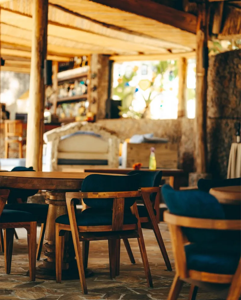 Wooden tables and blue-cushioned chairs under the thatched roof, with the stone bar behind them