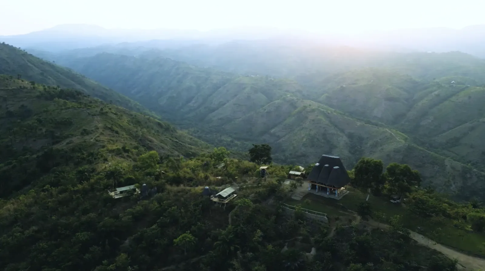 Les collines verdoyantes au-dessus du lac Tanganyika au lever du jour, vues du ciel, avec un belvédère au toit de chaume sur la crête