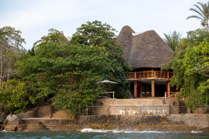 La villa Moonstone sous chaume au-dessus de sa terrasse en pierre, balcon en bois sous les larges avant-toits et transats installés parmi les rochers