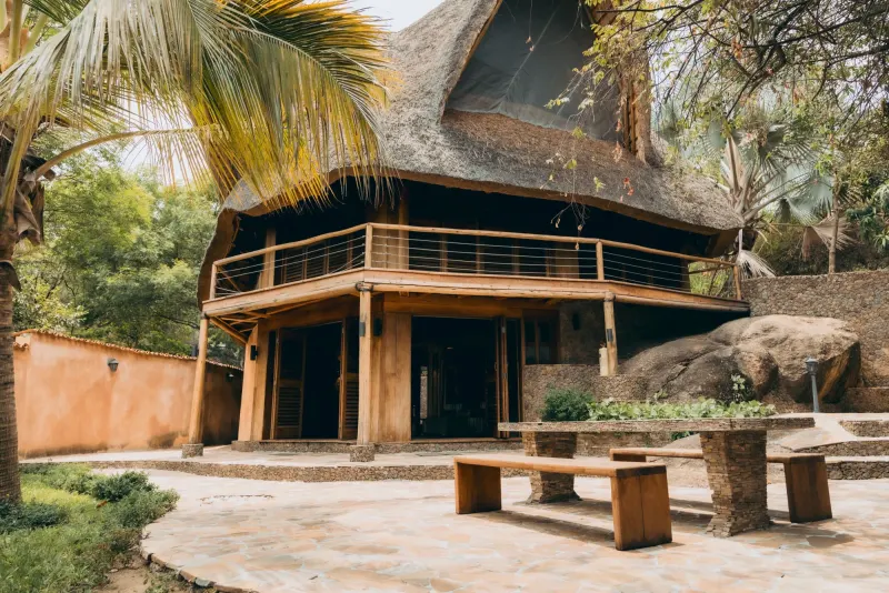 Une villa sous chaume adossée à des rochers de granit, sa terrasse ouverte meublée de transats et de fauteuils au pied des marches