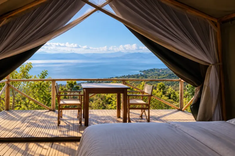 La vue depuis une tente perchée : deux chaises pliantes et une table sur la terrasse, les vallées verdoyantes au-delà et le soleil qui se couche derrière