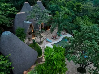 Une villa au toit de chaume avec sa piscine privée incurvée et sa terrasse, entourée de forêt